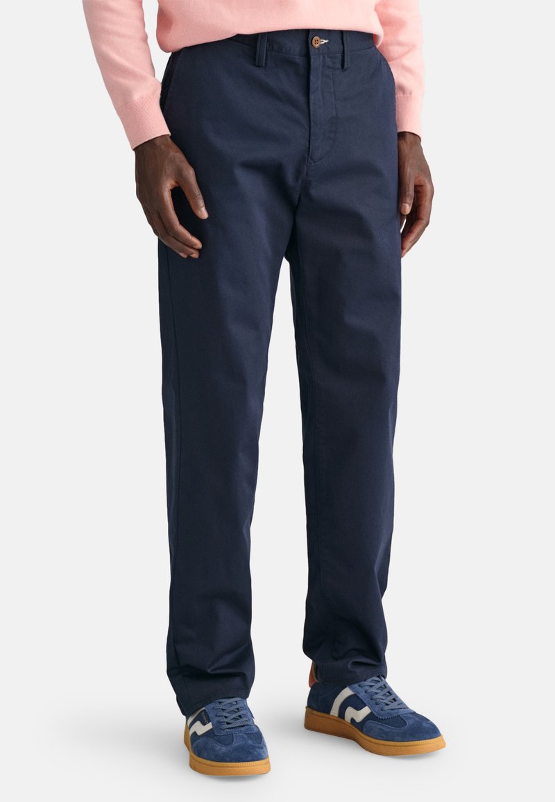Chinos azul marino hechos de algodón duradero, con un corte recto, cierre de botón y bolsillos laterales, combinados con zapatillas azules.