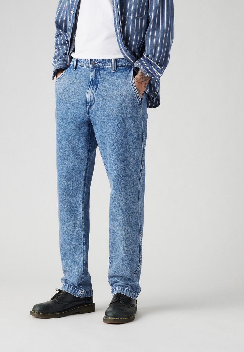 Helle blauen Jeans aus Denim mit geradem Schnitt, fünf Taschen und dezenten Nähdetails. Kombiniert mit schwarzen Lederschuhen.