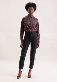 Jeans neri a vita alta con gamba dritta, abbinati a una camicia marrone con bottoni caratterizzata da una piccola stampa multicolore e un colletto.