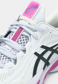 Λευκό αθλητικό παπούτσι Asics με ανοιχτό μπλε κορδόνια, μαύρο λογότυπο στο πλάι, ροζ και τιρκουάζ branding, και πλέγμα στην επάνω πλευρά για αναπνοή.