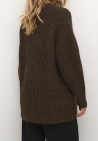 Brun, fluffig stickad tröja med avslappnad passform, långa ärmar och en lätt rundad nederkant, texturerat material och utan märkbara detaljer eller mönster.