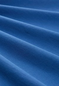 Blått tyg med en texturerad väv, som har mjuka veck och en slät yta. Materialet verkar hållbart och jämnt färgat.