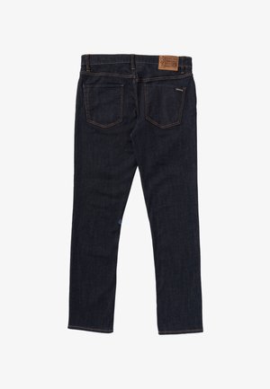 Jean en denim bleu foncé vu de dos avec deux poches arrière, des passants pour ceinture, et un patch de marque en cuir marron sur la ceinture.