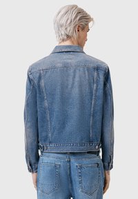 Jeans jakna u svijetloplavoj boji klasičnog kroja, s kopčama, dva stražnja šava i skraćenim rubom. Tekstura izgleda blago istrošeno.