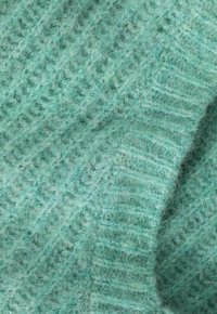 Tissu tricoté turquoise avec un motif texturé, présentant des fibres douces et duveteuses ainsi qu'un design à côtes. Matériau chaud et léger.