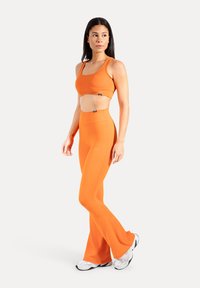 Oranssi urheilurintaliivit ja levenevät leggingsit joustavasta materiaalista. Suunnittelussa saumattomuus ja vähäiset metalliosat.
