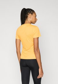 Żółta, dopasowana koszulka z krótkim rękawem wykonana z gładkiej tkaniny, z okrągłym dekoltem i prostym wzorem, zestawiona z czarnymi legginsami.