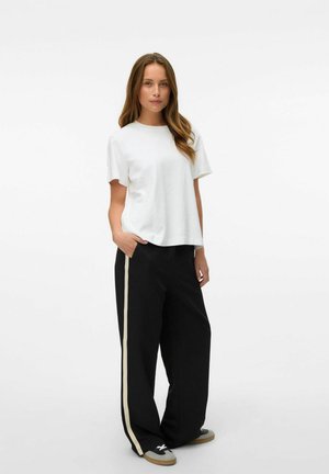 White cotton t-shirt with short, slightly rolled sleeves, paired with black wide-leg trousers featuring a beige side stripe and gray sneakers.