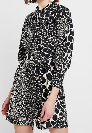 Frau trägt ein langärmliges schwarz-weißes Kleid mit Tierdruck, Taillengürtel und Knopfleiste vorne.