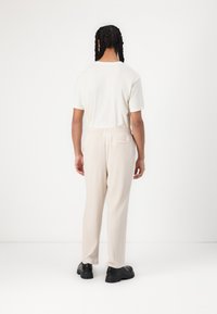 Beige geribde broek met een elastische tailleband, gecombineerd met een witte t-shirt met korte mouwen. Zwarte chunky schoenen maken de outfit compleet.