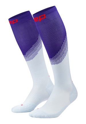 Paar knielange Sportsocken mit weißen Füßen und Unterschenkeln und violettem Oberschenkel mit rotem Text nahe oben.