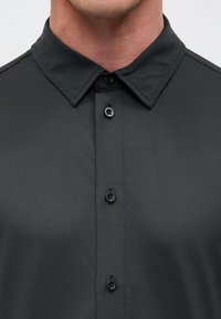 Donkergrijs shirt met een klassieke kraag, voorzien van een knoopsluiting aan de voorkant, een gladde textuur en subtiele stikseldetails.