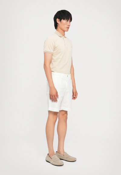 Beige polo-skjorte med tekstur, hvite skreddersydde shorts og beige loafers. Enkelt design, korte ermer og krage.