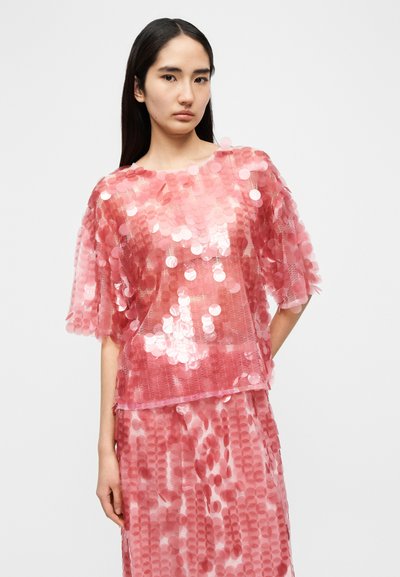 Haut rose à sequins avec manches courtes et col rond, présentant des motifs circulaires en sequins et une coupe ample.