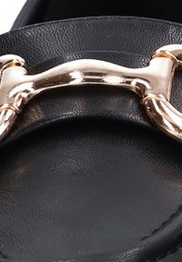 Mocasines de cuero negro con un prominente detalle de cadena de metal dorado en la parte frontal, que destacan por su textura suave y diseño limpio.