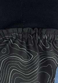 Un materiale di maglia nera nella parte superiore si trasforma in un tessuto nero con linee di contorno bianche. La parte inferiore presenta un accento blu lungo il bordo.