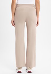 Pantalons larges beige clair en tissu lisse, dotés d'une taille haute et d'un léger éclat. Associés à des baskets blanches et beiges.