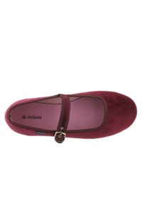 Bailarina de ante roja con una correa ajustable, hebilla en tono dorado, punta redondeada y una plantilla suave de color rosa, que presenta un logo sutil en el lateral.
