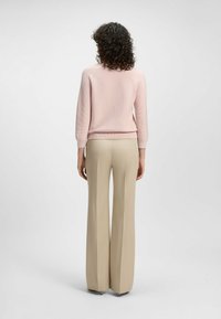 Różowy sweter wykonany na drutach z rękawami do 3/4, zestawiony z beżowymi spodniami o wysokim stanie, charakteryzującymi się prostym krojem i długą sylwetką.