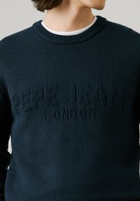 Tamsiai mėlynas megztinis su tekstūruotu logotipu "PEPE JEANS LONDON" iškilniai pavaizduotu priekyje. Apvalus kaklas ir raukiniai ant rankovių.