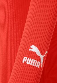 Gros plan d’un tissu côtelé rouge avec le logo Puma brodé en blanc et un puma sautant sur une manche.