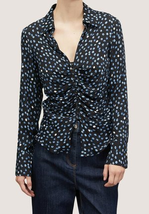 Camisa negra de manga larga con lunares azules y blancos, con fruncido en el frente, cierre de botones y cuello clásico. Textura de tela suave.