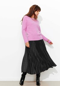 Pull rose duveteux à manches longues associé à une jupe noire plissée ornée de taches argentées. Des bottes noires montantes complètent la tenue.