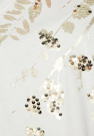 Witte stof met een bloemenpatroon versierd met metallic gouden en zilveren pailletten, wat een textuur en sprankelend effect creëert.
