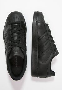 Baskets en cuir noir avec un embout texturé, six paires d'œillets, et des accents cousus sur les côtés pour plus de détails.