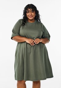 Olivgrön, mjuk t-shirtklänning i bomull med korta ärmar och en avslappnad passform, utrustad med sidfickor och rund halsringning.