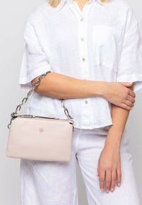 Borsa a tracolla in pelle rosa chiaro con finitura testurizzata, dotata di una tracolla in metallo argentato e chiusura a zip, esposta su uno sfondo neutro.