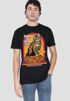 Young man wearing black t-shirt with a cat sitting on a communication board and text "Talk to your Cat" and a speech bubble with explicit language.