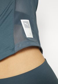 Närbild av en person som bär en blå Puma-idrottströja med en synlig Puma-logotyp nära fållen och matchande blå byxor.