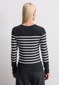 Svart langermet topp med hvite horisontale striper, med rund halsringning og slim fit. Glatt stoff uten synlige mønstre eller dekorasjoner.