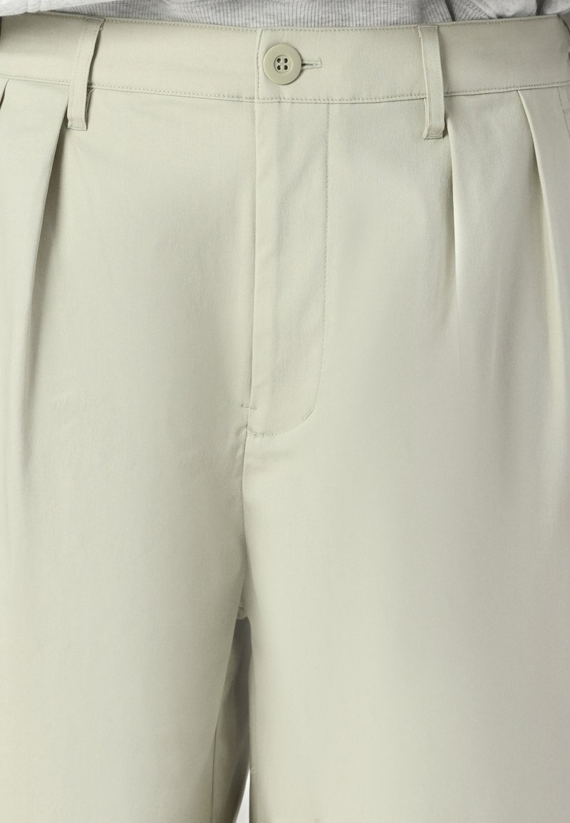 Beige gefaltete Hose aus glattem Stoff, mit einem einzigen Knopfverschluss und Seitentaschen, in strukturierter Passform und mit sauberen Kanten.