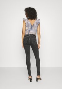 Top de tela ligera con mangas acampanadas y un diseño estampado en azul, combinado con jeans negros de cintura alta y sandalias de tacón negro.