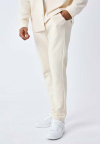 Crème-kleurige joggerbroek met een gestructureerde afwerking, voorzien van zijzakken en een taperende pasvorm, gecombineerd met witte sneakers.