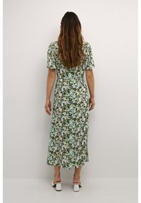 Blumenmuster, Midikleid in Grün, Blau und Weiß. Kurze Puffärmel, taillierter Oberteil und fließender Rock. Weiße Blockabsatzschuhe.