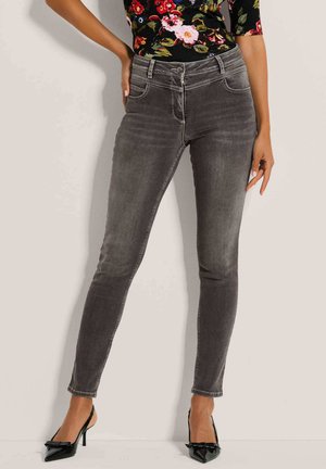 Graue, schmal geschnittene Jeans mit leicht ausgewaschenem Finish, fünf Taschen und Reißverschluss. Kombiniert mit schwarzen High-Heels.