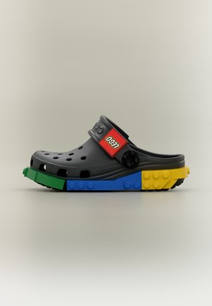 Sabot style Croc noir avec semelle en briques LEGO vertes, bleues et jaunes et logo LEGO rouge sur la bride noire réglable.