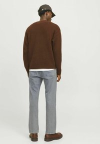 Jersey de punto marrón con un corte relajado, combinado con jeans de denim azul claro y zapatos marrones. Una gorra oscura completa el conjunto.