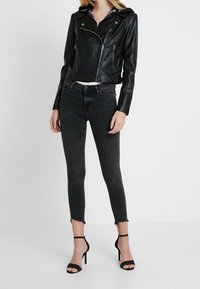 Zwarte leren motorjack met ritsen, gecombineerd met donkergrijze skinny jeans met rafelige zoom en zwarte hakken met banden.