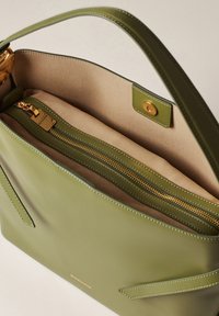 Grüne Lederhandtasche mit glatter Textur, ausgestattet mit einem goldenen Reißverschluss und einem beigen Innenfutter. Enthält zwei seitliche Taschen und einen Druckverschluss.