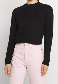Suéter negro de canalé con cuello redondo y mangas largas, combinado con jeans rosa claro de talle alto. Textura suave y estilo ajustado.