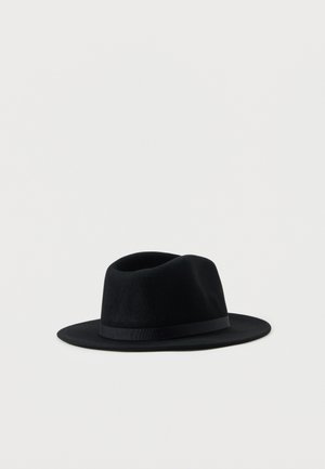 Sombrero fedora de fieltro negro de ala ancha con una cinta negra, sobre un fondo gris claro liso.