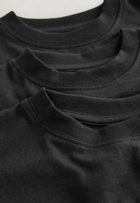 Tri čierne bavlnené tričká naskladané na sebe, s lemovanými okrúhlymi výstrihmi, hladkou textúrou a viditeľným šitím okolo goliera.