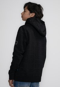 Felpa nera con design testurizzato che presenta motivi ripetuti. Ha una tasca a pouch, cappuccio regolabile e polsini a costine.
