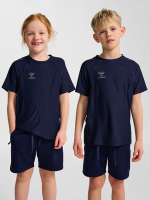 Zwei Kinder, die passende marineblaue Hummel-Sportshirts und Shorts tragen, stehen nebeneinander vor einem schlichten Hintergrund.