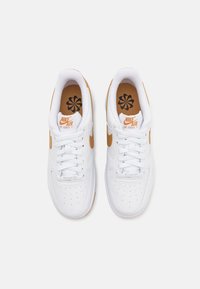 Paire de baskets blanches Nike Air Force 1 avec le swoosh et le logo orange, vues de dessus sur un fond clair uni.
