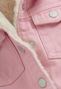 Veste en jean rose avec boutons pression argentés et doublure en polaire blanche visible le long des bords et à l'intérieur du col.